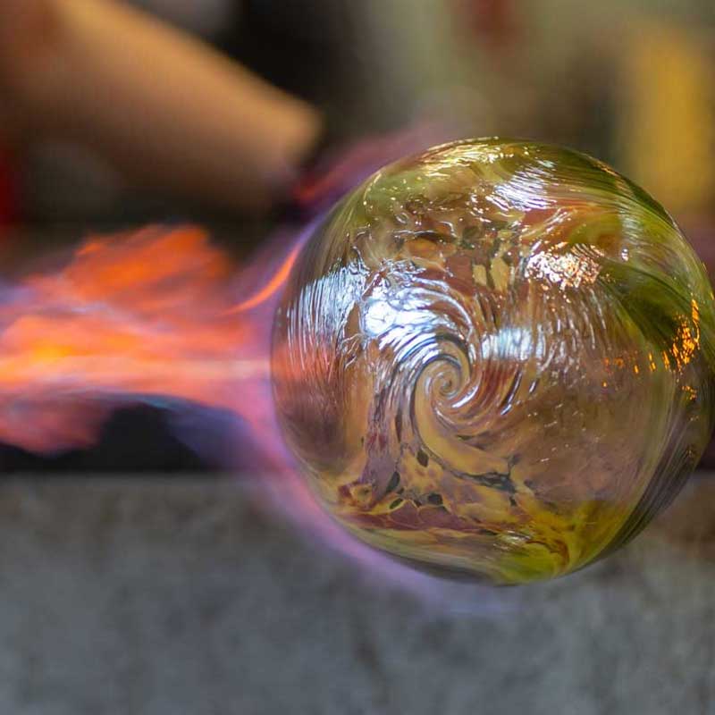 A glassblower puts a flame to their art in progress.
