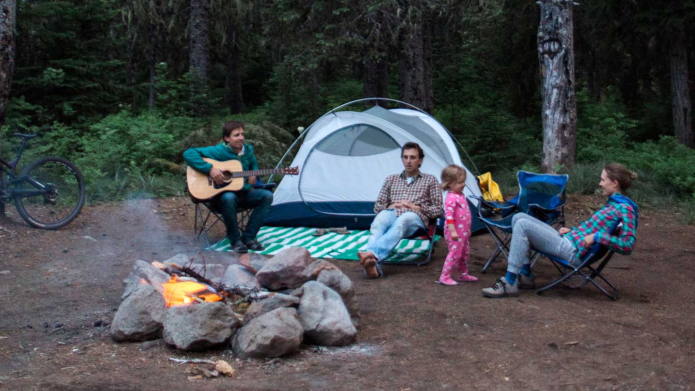 A family sits around a fire at a campsite.
