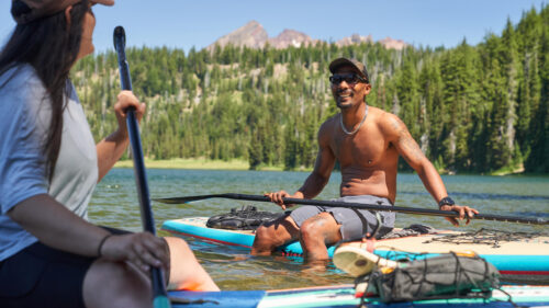 man sits on paddleboard holding paddle on lake