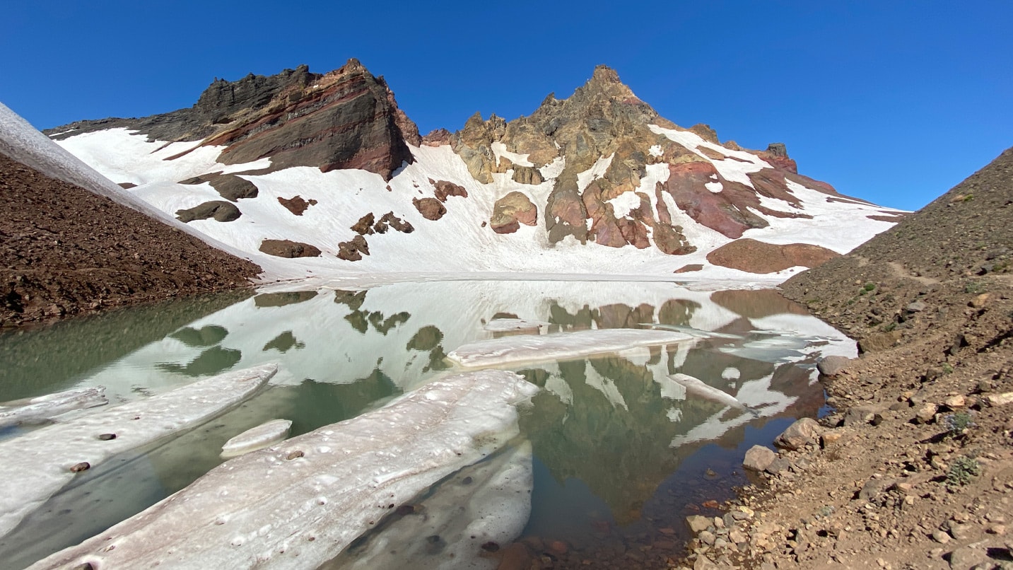 Snowmelt surrounds a high-altitude alpine lake.