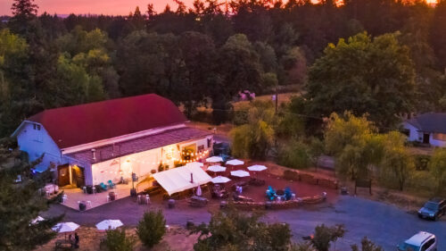 An aerial view of a farmhouse building and outdoor patio at sunset.