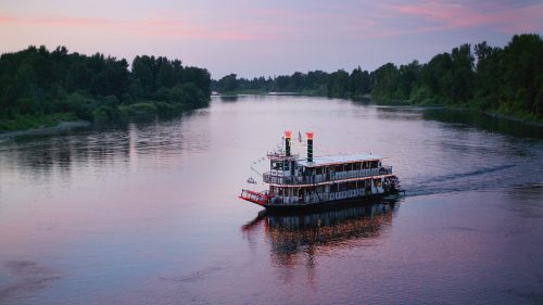 A paddlewheel boat glides across the river at sunset