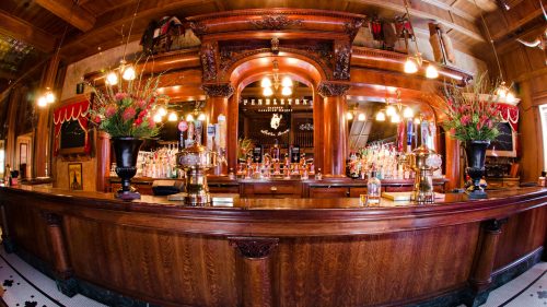 A mahogany bar is lined with bouquets of flowers and lights.