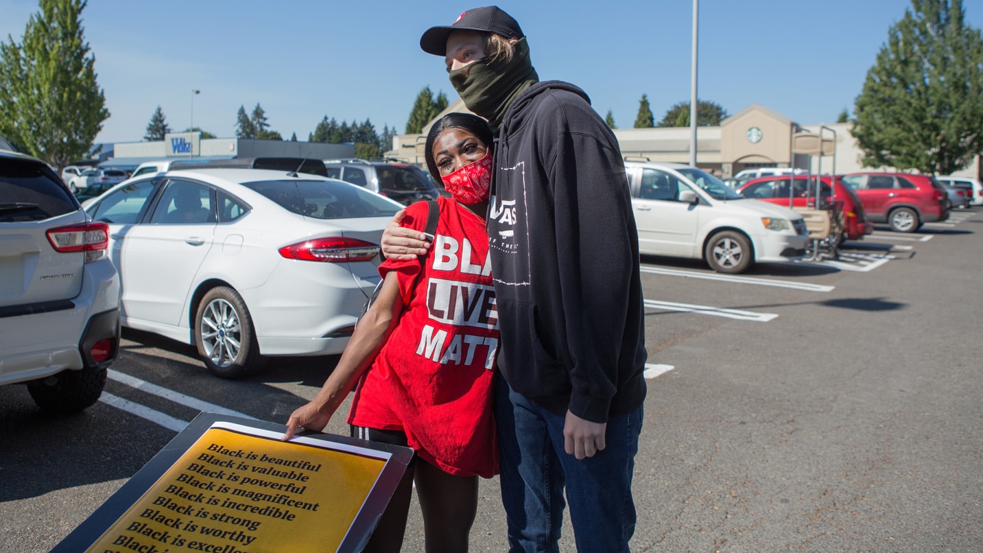 Two masked people hug in a parking lot.