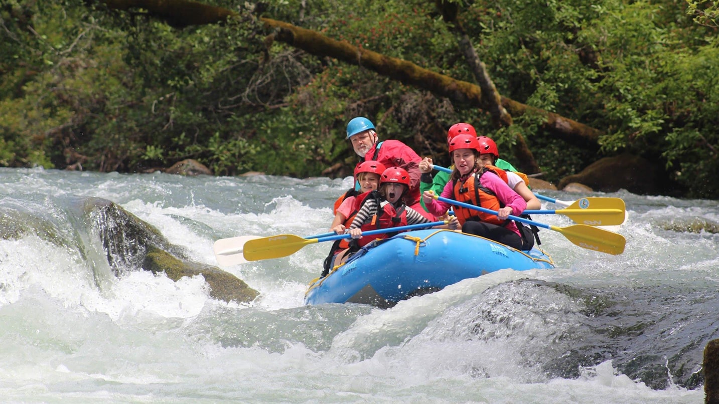 A raft full of people travels over a river rapid