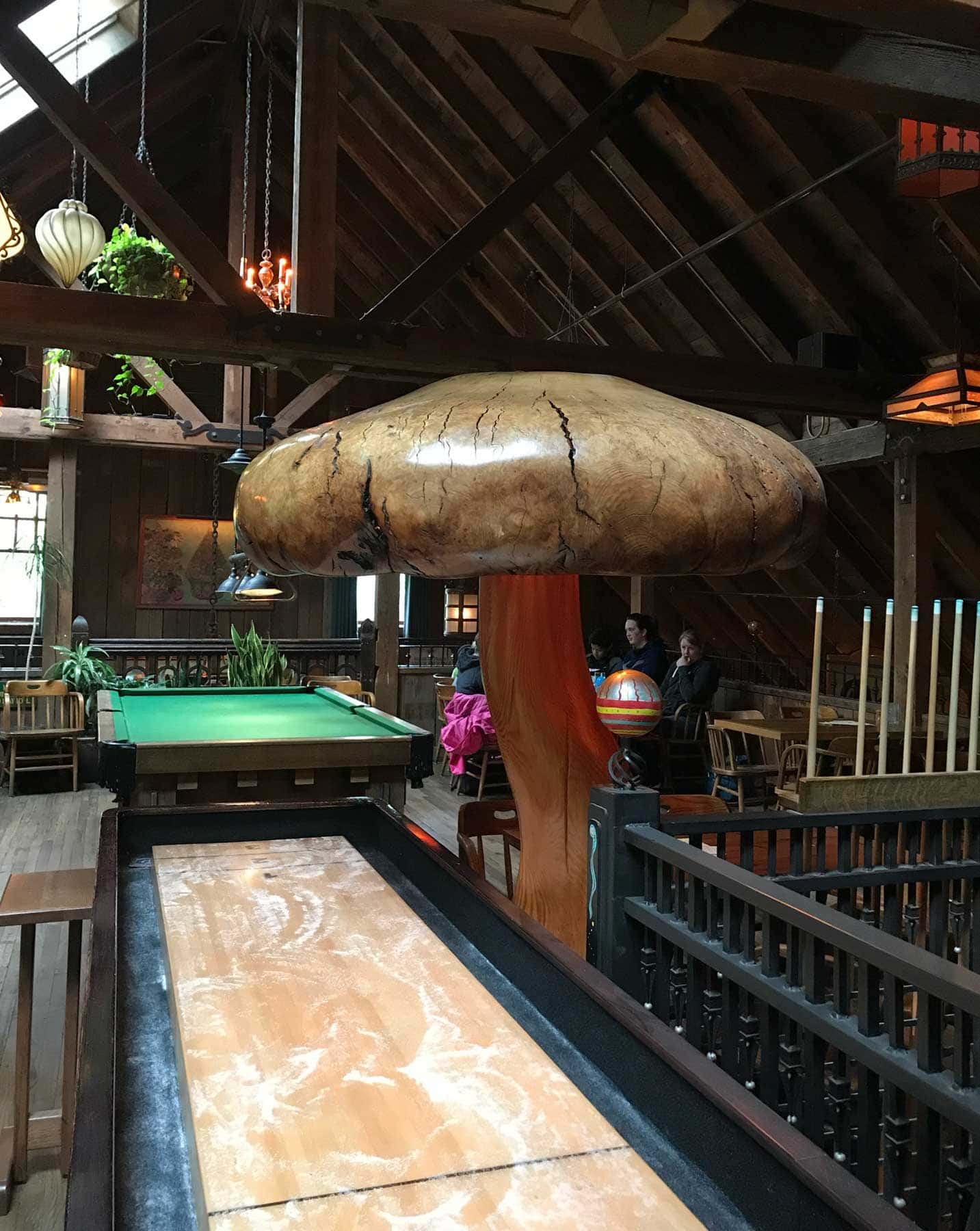 A large mushroom statue leans towards a billiards table.