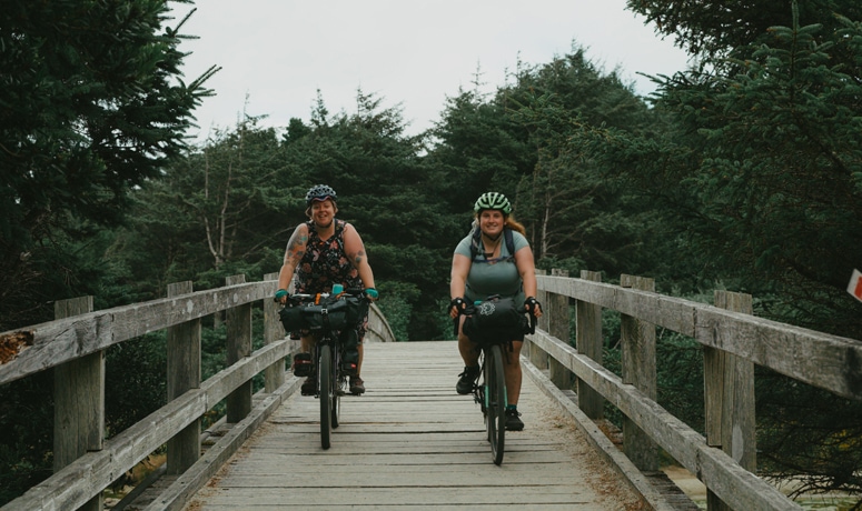 two bicyclists riding over wooden bridge