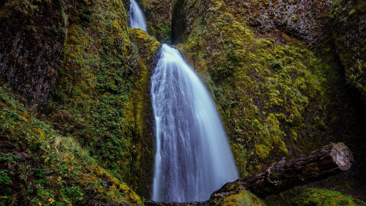 A two-tiered waterfall flows over a mossy cliff