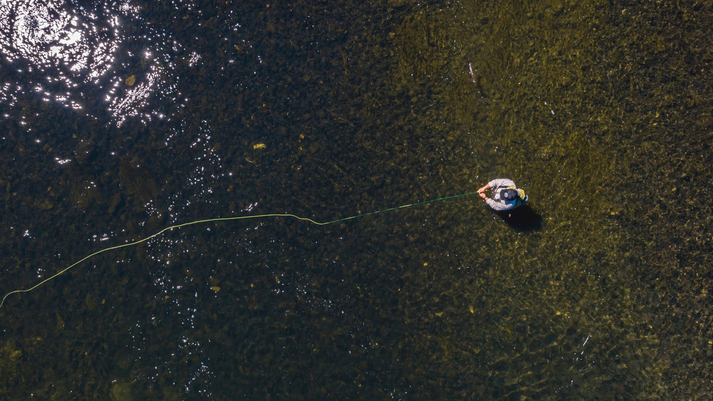 An overhead photo of a person fly fishing in a clear river