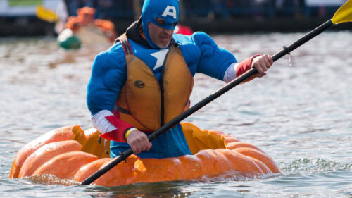 A man in costume paddles inside a giant carved out pumpkin