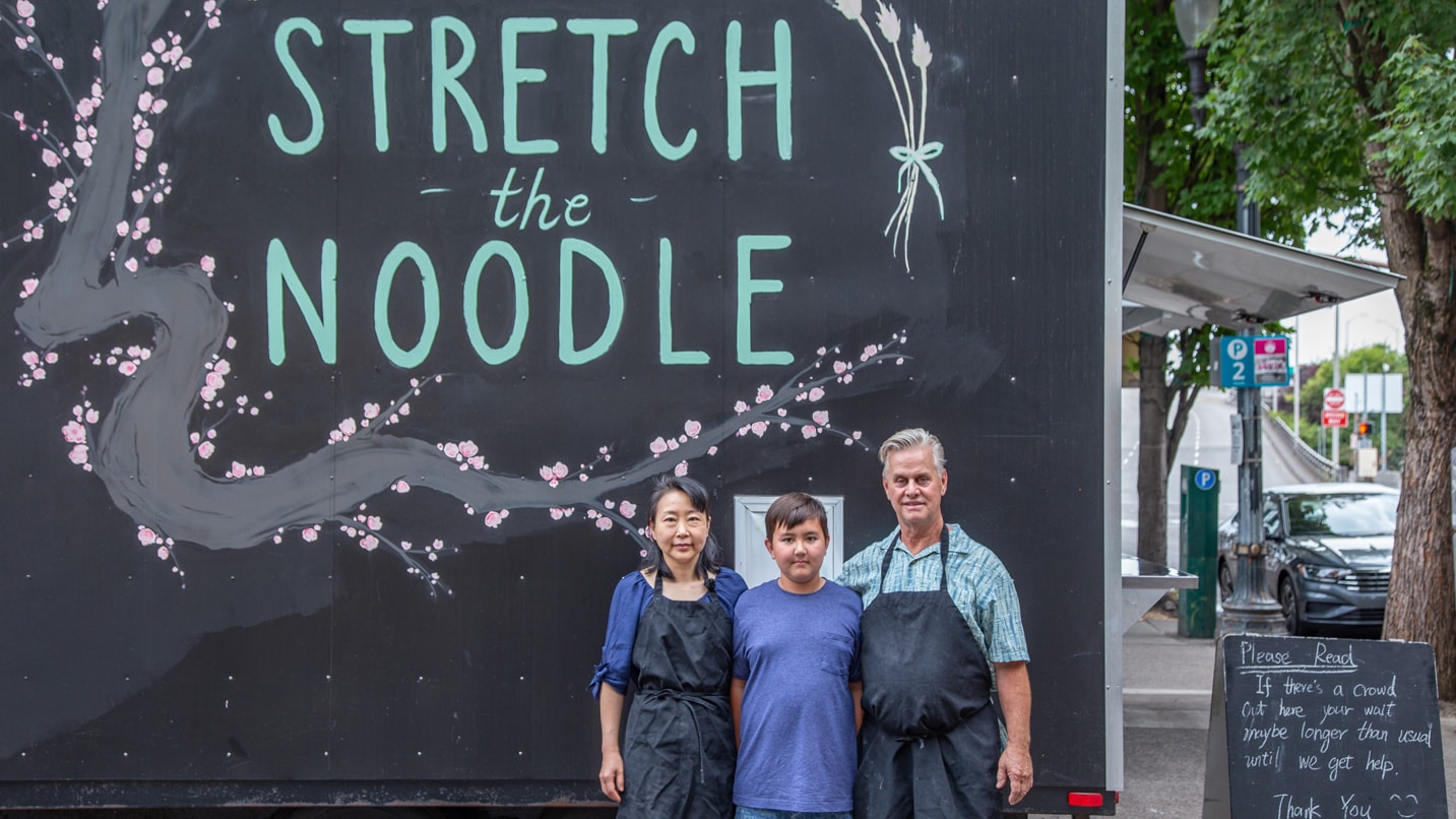 Stretch the noodle cart owners stood in front of their food cart.