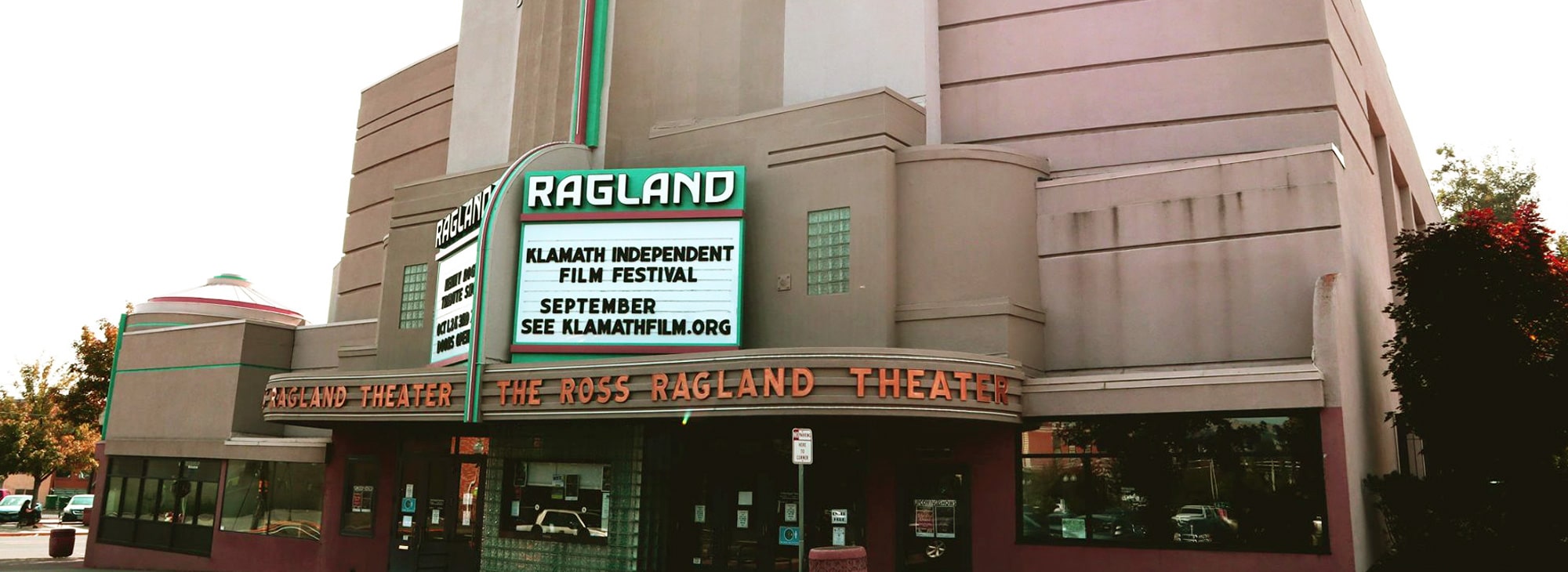 Marquee displays event details on theater façade. Text reads: "KLAMATH INDEPENDENT FILM FESTIVAL SEPTEMBER SEE KLAMATHFILM.ORG." Context: Historic building with art deco design elements in urban setting.