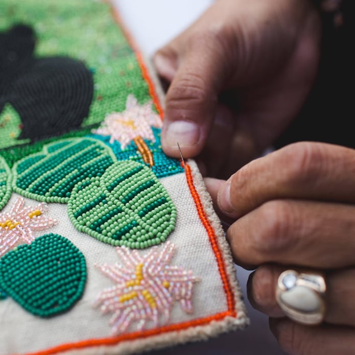 Hands of an Indigenous person making bead art.