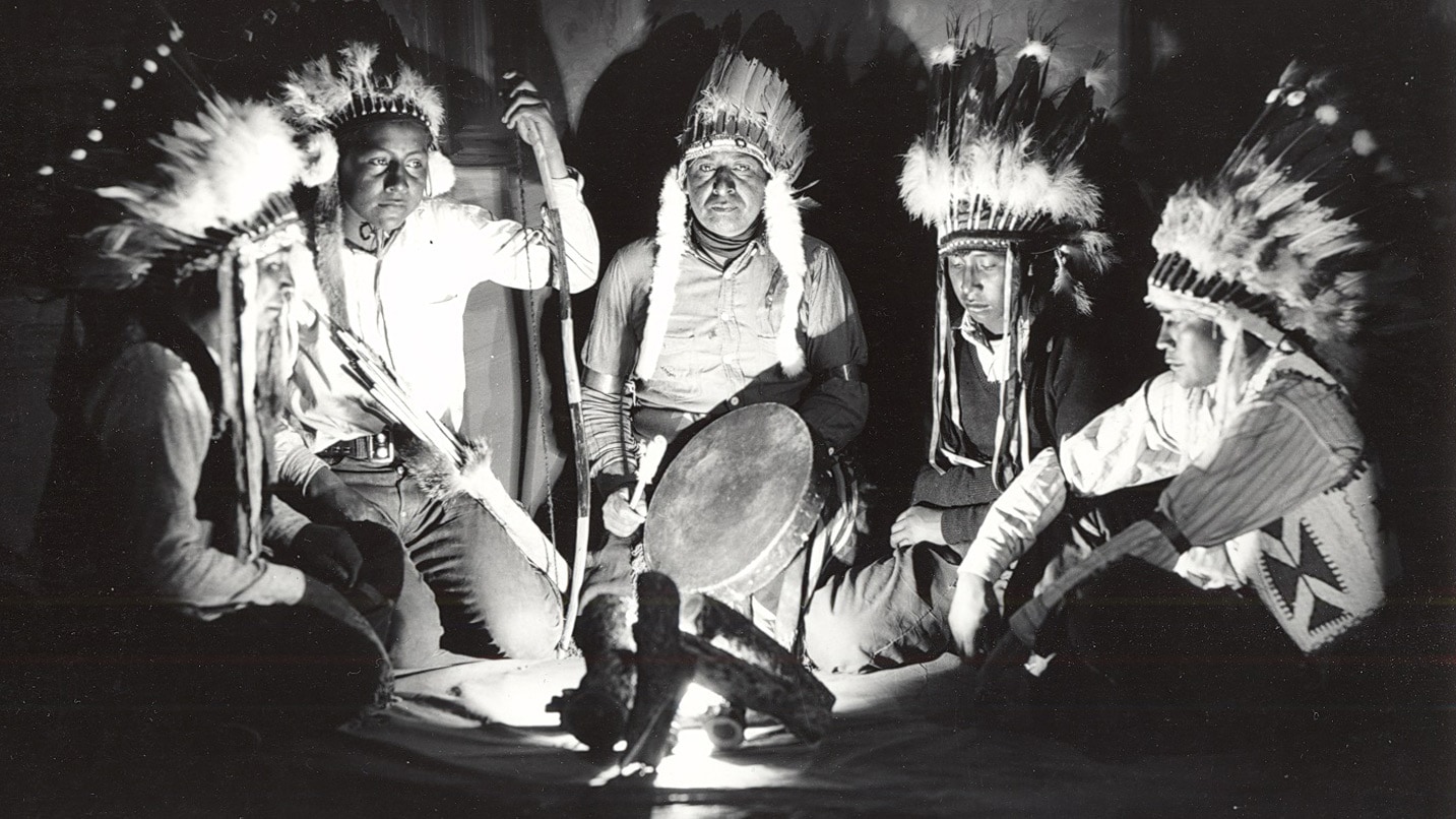 Native Americans in traditional headdresses sit in a circle