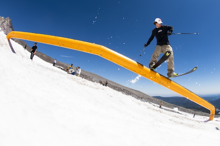 A skier does a trick on a pipe above a snowy mountain