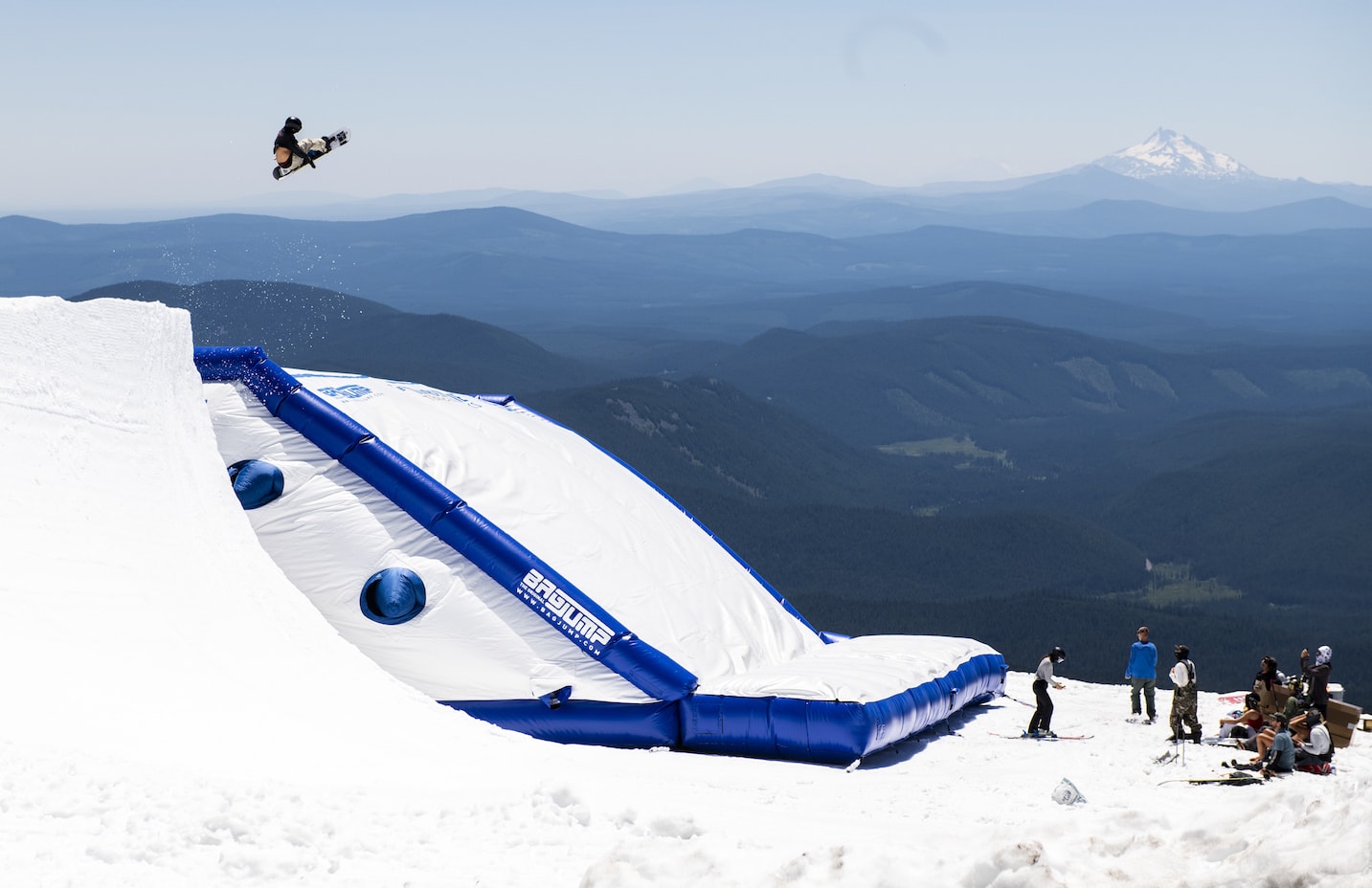 A skier does a trick high above an airbag on a snowy mountain