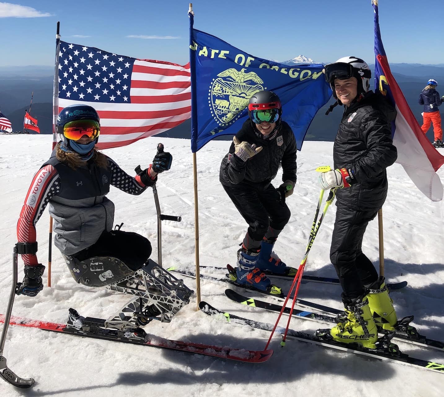 Three skiers pose with flags on the snow