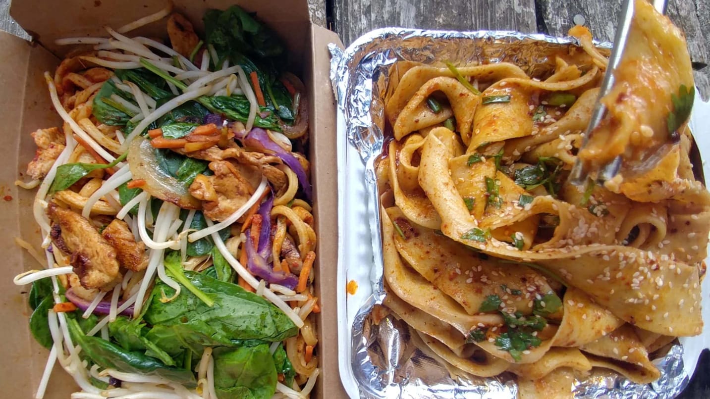 two containers of noodle dishes with colorful veggies