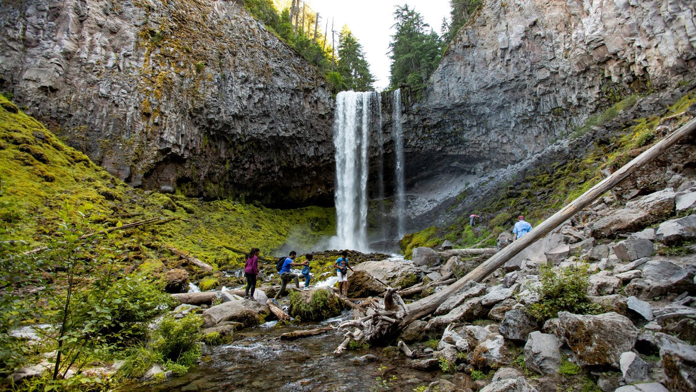 Hikers are in the foreground of a tall waterfall