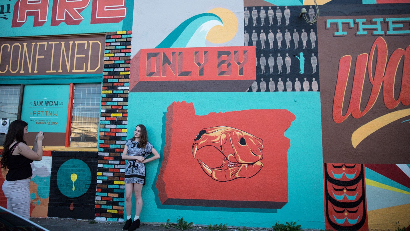 A woman stands next to a mural of the shape of Oregon