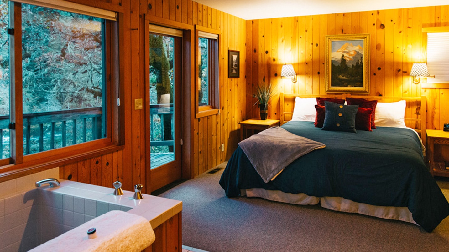 A cozy bed is and tub are in a wood-paneled room