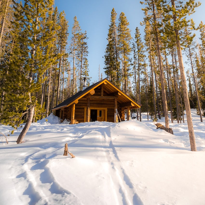A snowy trail leads to a log cabin warming shelter