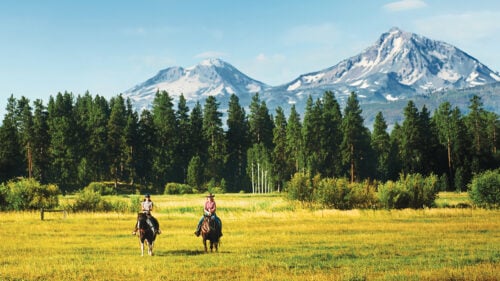 Two people on horseback in front of snowy peaks