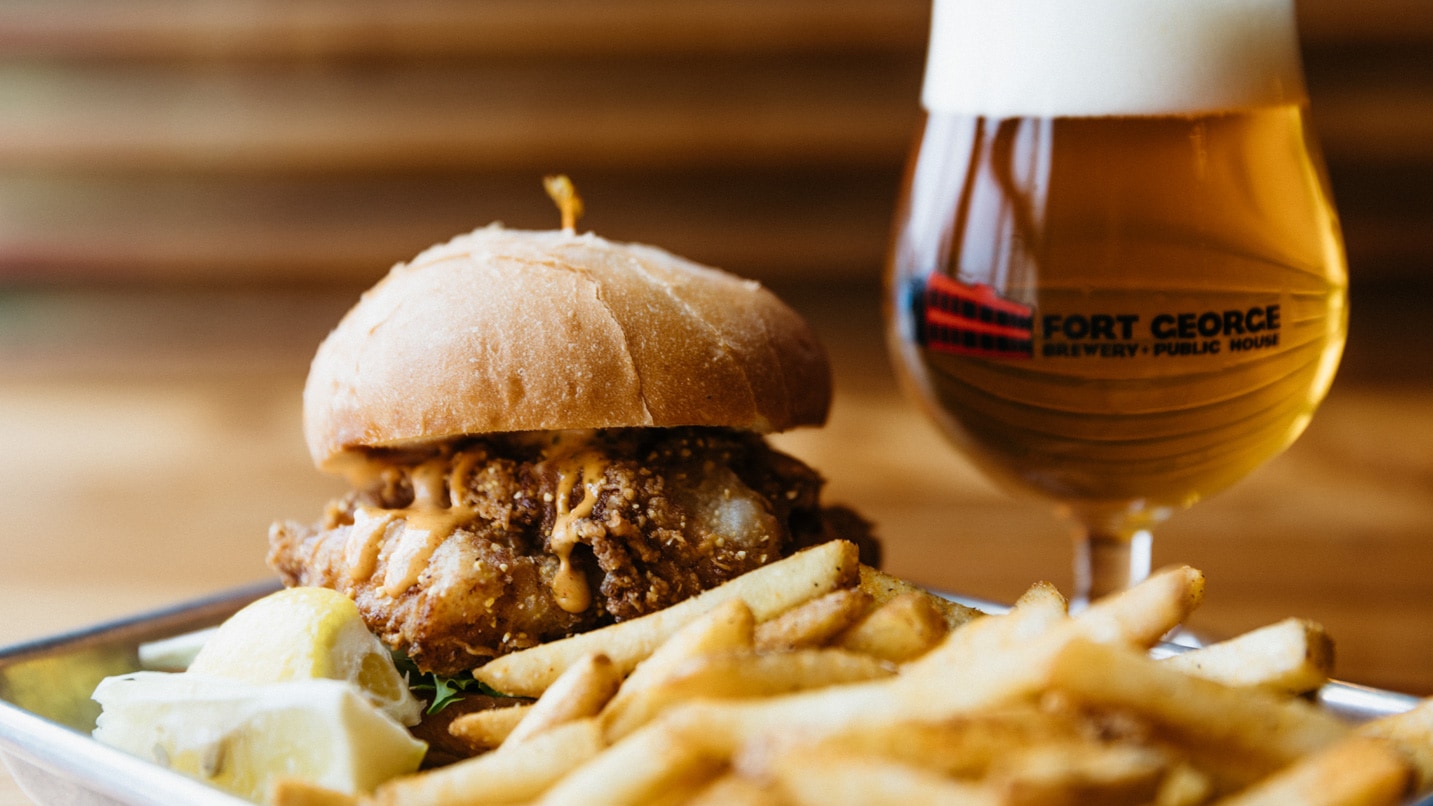 Close-up of beer in glass and chicken burger on bun with fries
