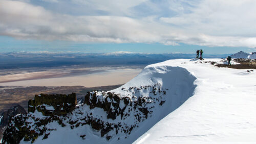 Two people stand on the edge of a snowy cliff