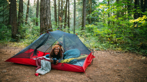 A woman smiles while peeking out of a tent in a forest