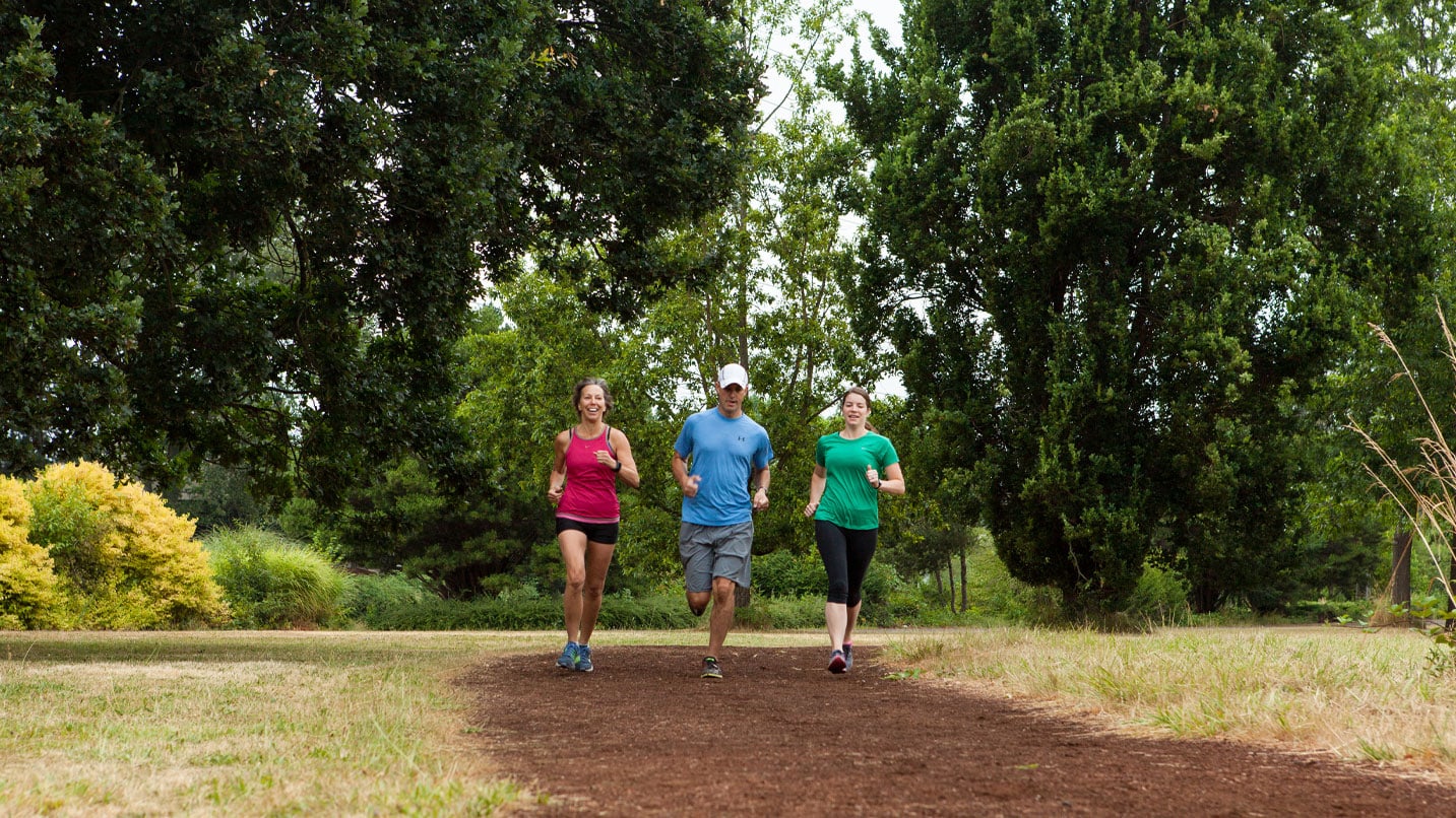 Three people run along a flat trail