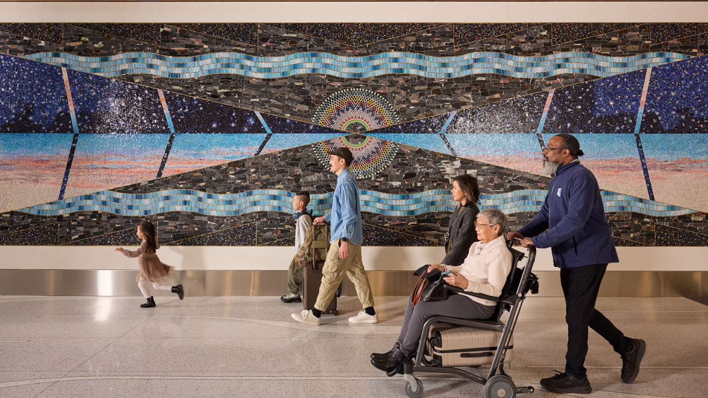 People passing by a coloful art mural on display at the Portland airport.