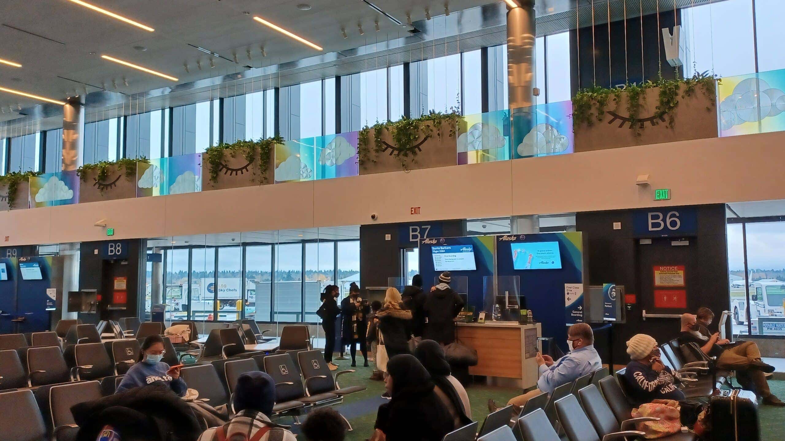 People sit on chairs at the airport, with rows of large windows