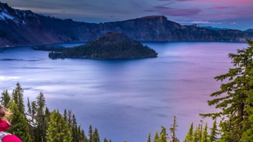 A woman looks at the view of Crater Lake during sunset
