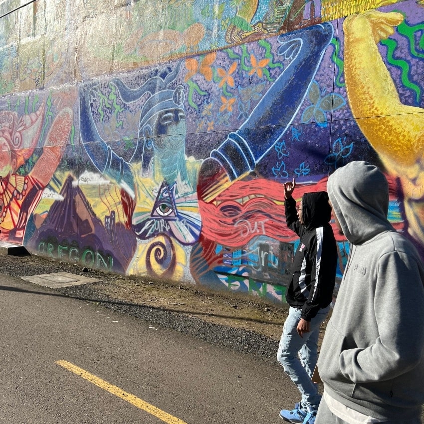 Two boys stand beside a colorful mural
