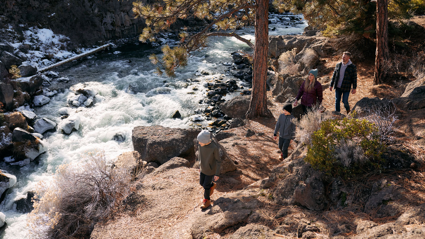 People walking a rocky dirt path alongside river rapids.