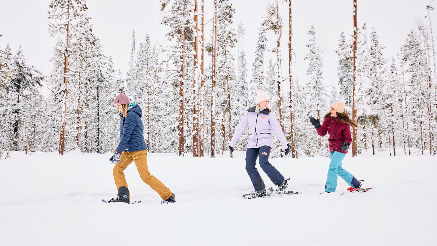 Three women snowshoeing through a forest.