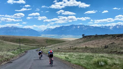 cyclists ride on road toward mountains and blue sky