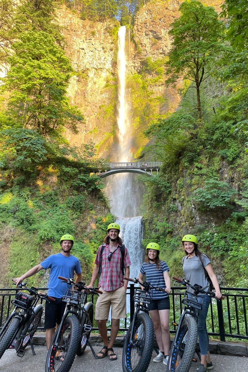 A group of cyclists stand in front of a tiered waterfall