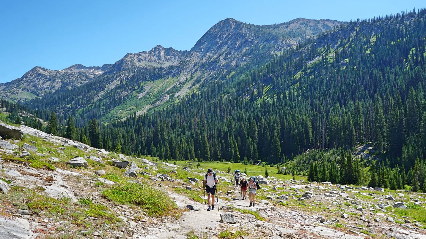 A group of people hike down a trail with the mountains in the distance