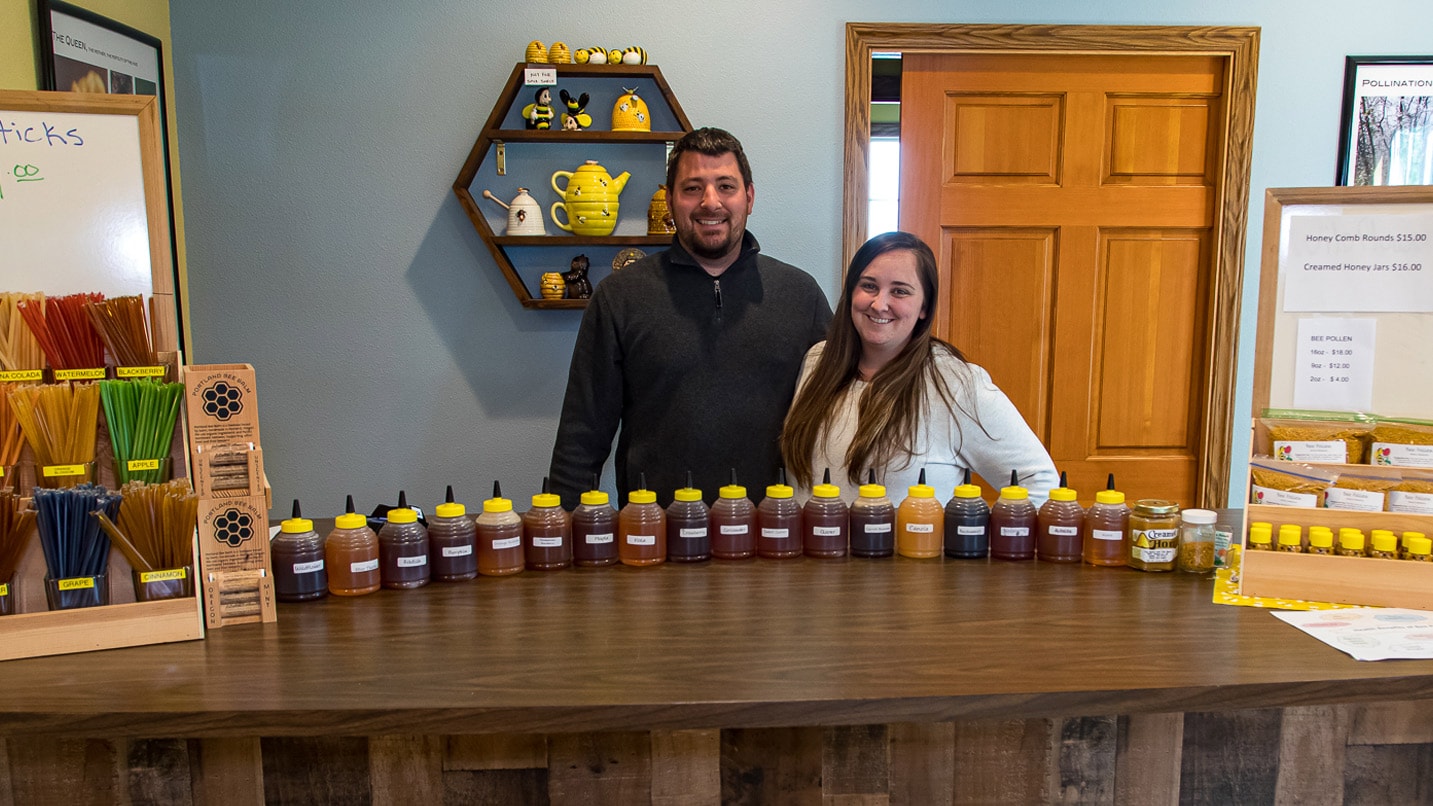 Two people stand behind a counter lined with jars of honey