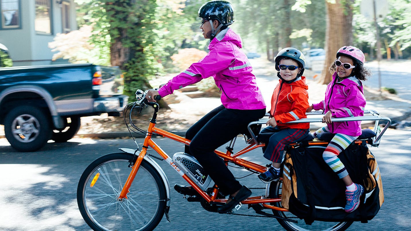 A person and two children ride on a bike with brightly colored jackets