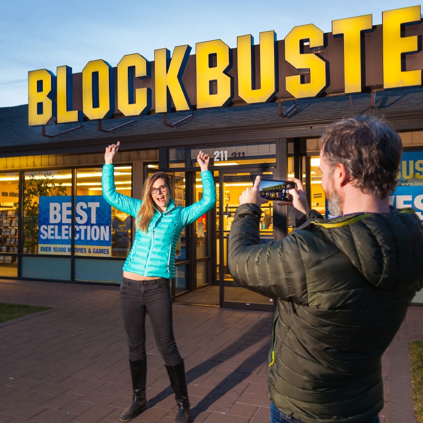 A person poses for a photographer in front of a Blockbuster sign
