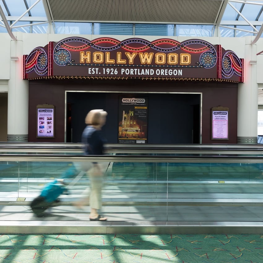 A person rides down an airport's walkway in front of an entrance to a theater