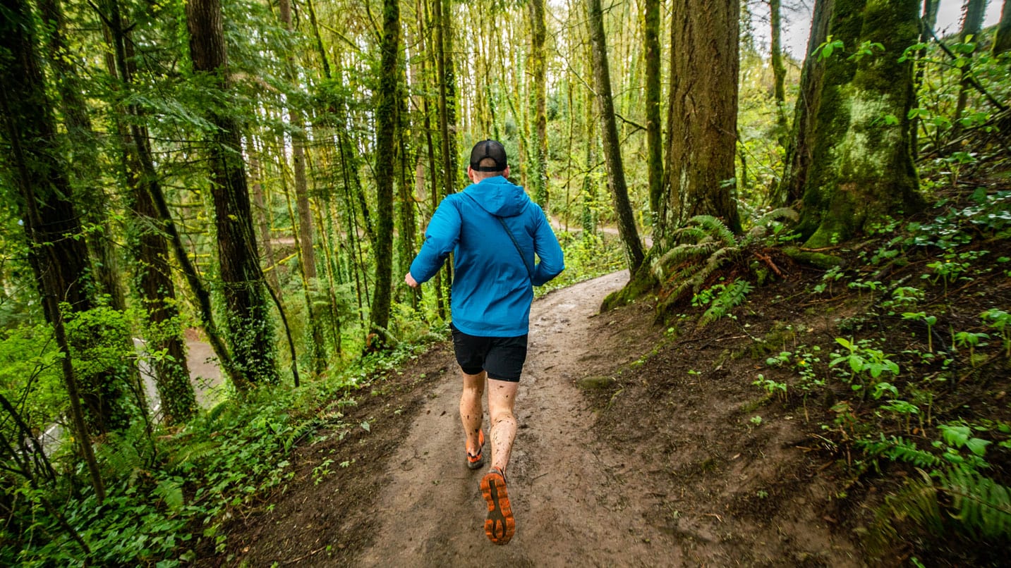 Man runs on single muddy trail in a wooded area