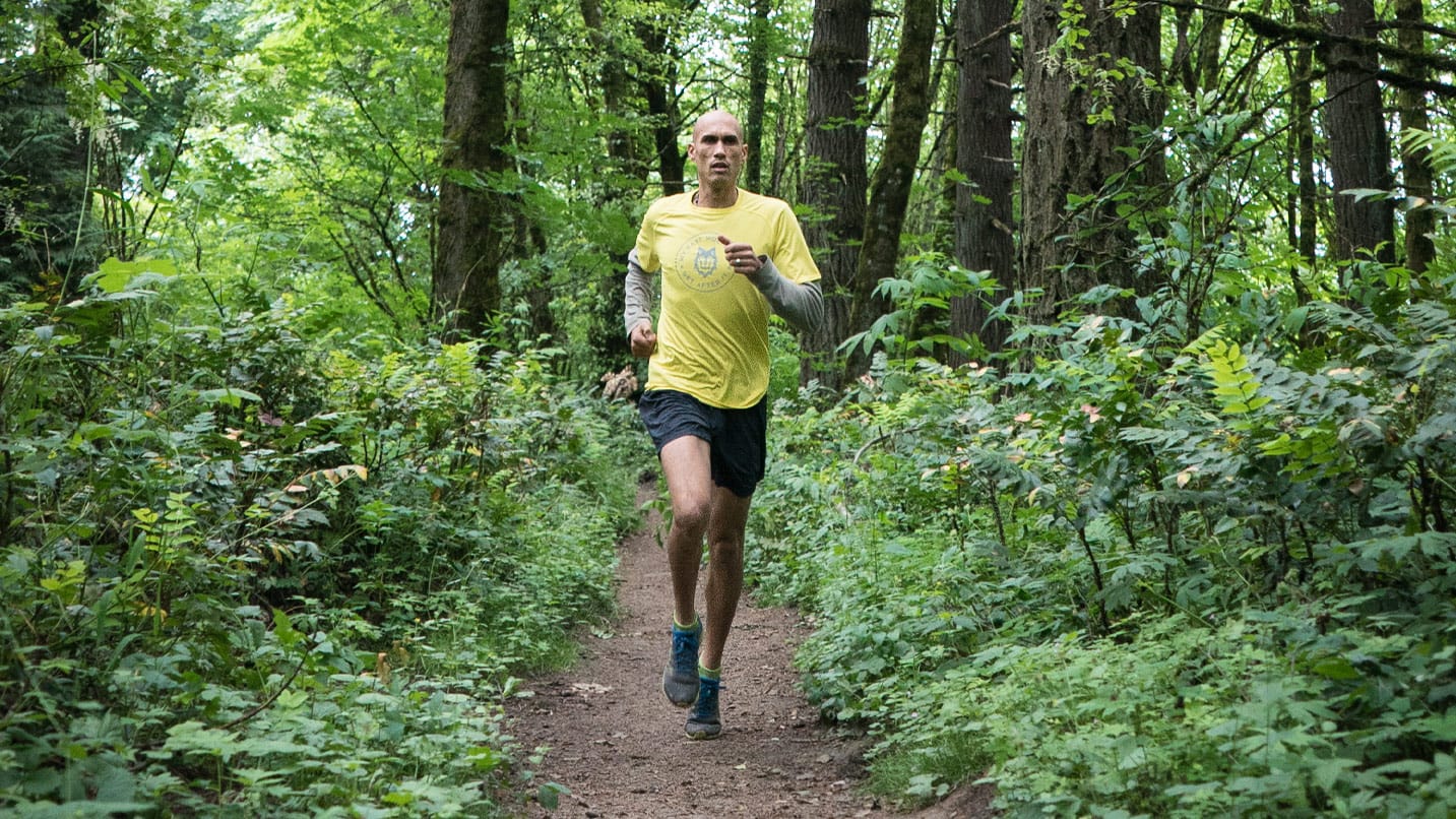 Man runs along single track trail in a wooded area.
