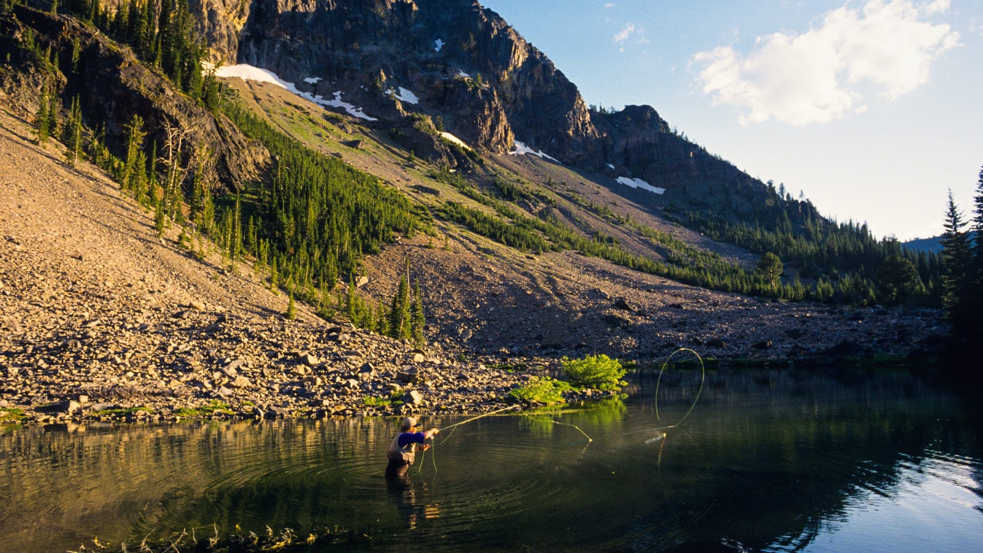 A person fishing in a small lake at the bottom of a mountain