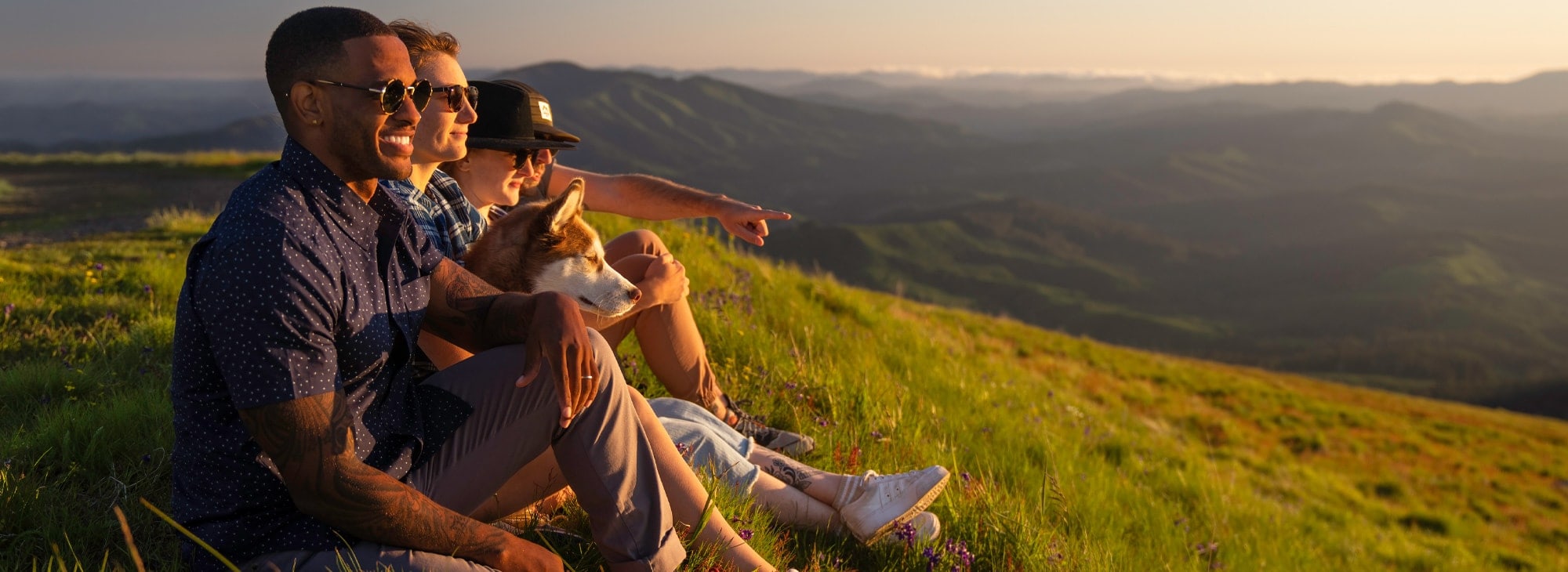 People sit on a hillside at sunset