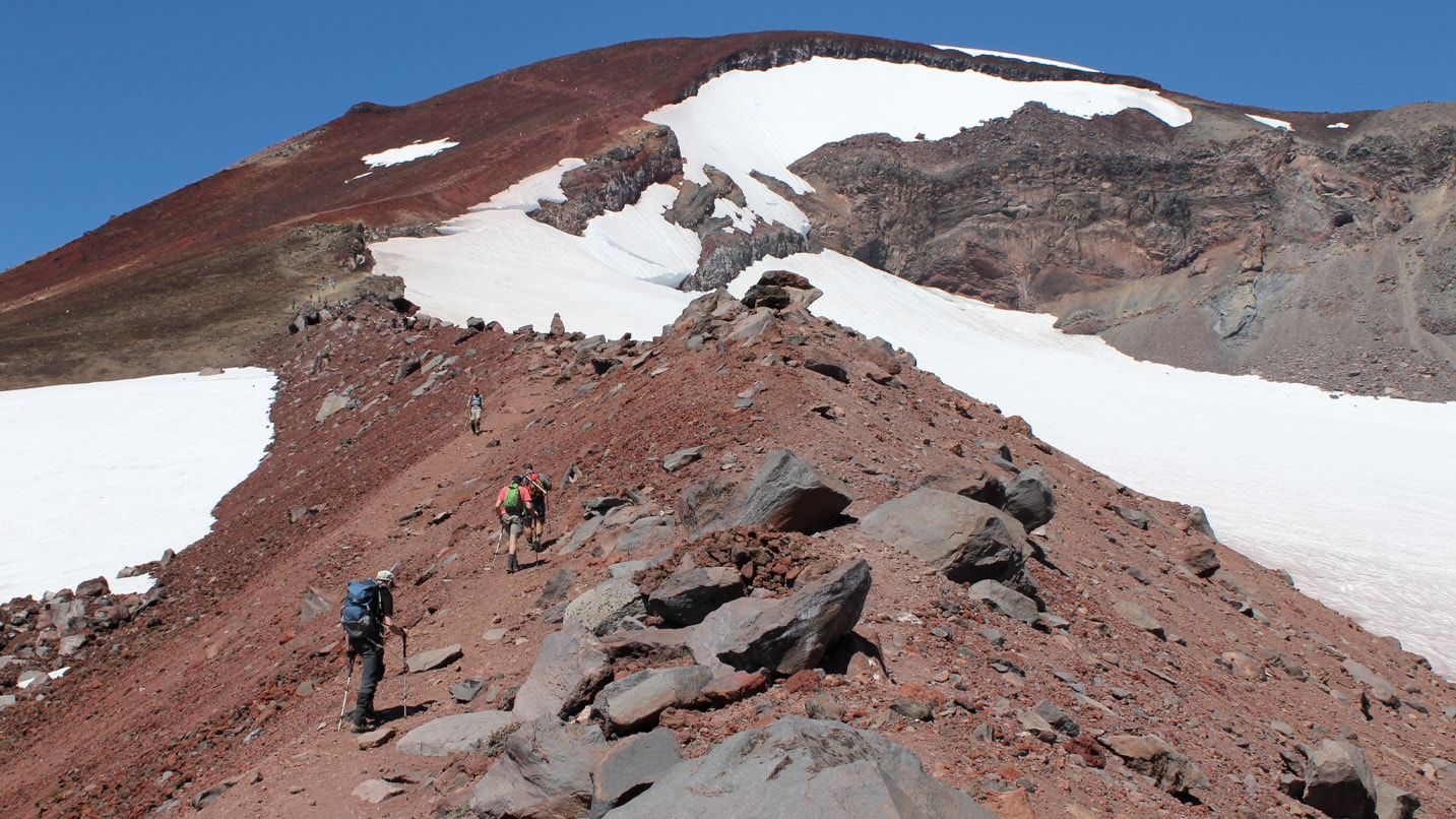 People hiking up a rocky mountain with patches of snow