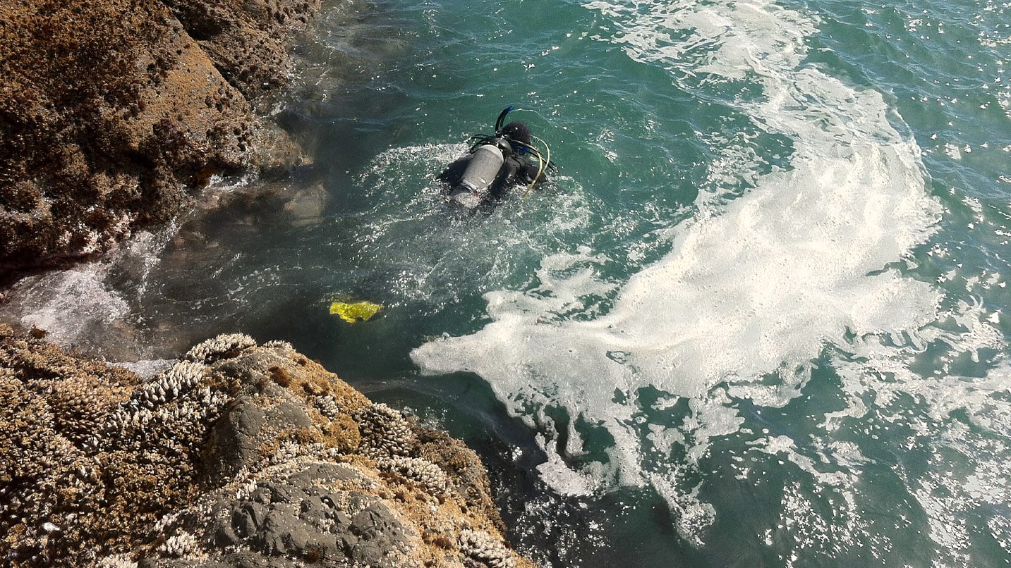 scuba diver in blue water near rocky cliff